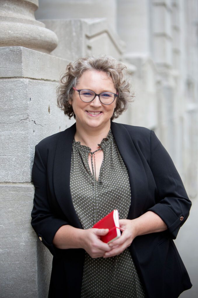 Photographie de Veronique Cyr, consultante de CYR Communication, prise dans le Vieux-Québec en juillet 2023. Véronique tient dans ses mains le carnet rouge dans lequel elle prend des notes lorsqu'elle connecte en personne.